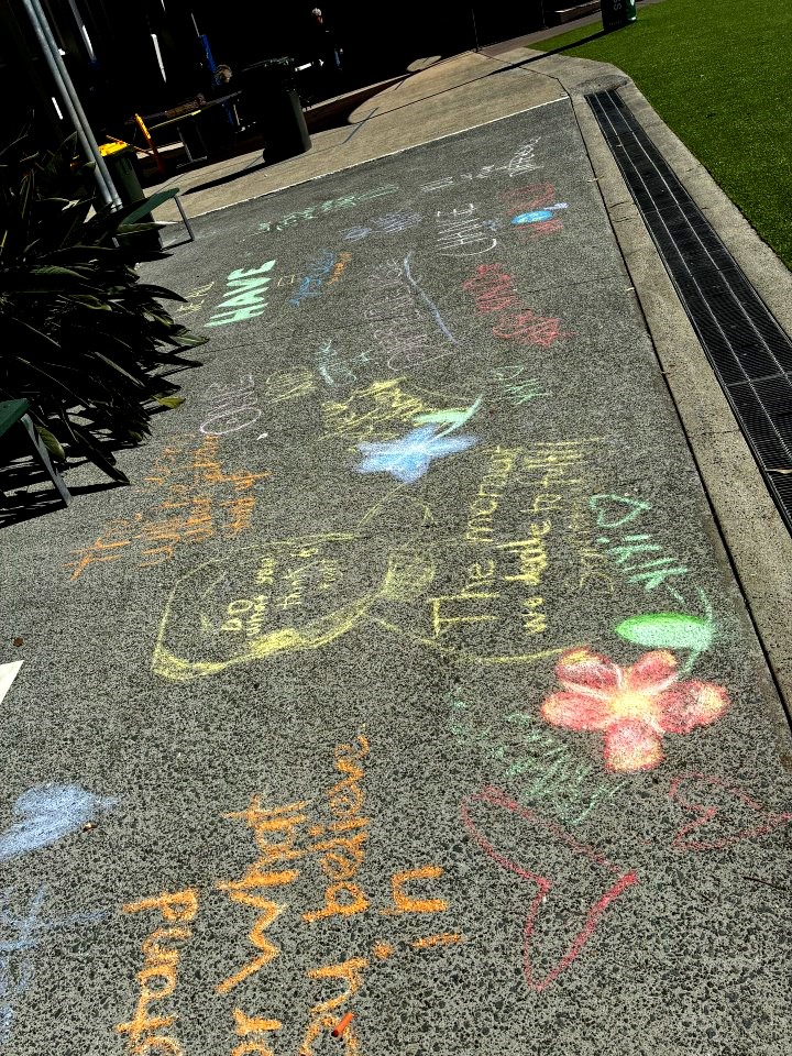 Colourful chalk drawings and messages cover a school pathway during Mercy Formation Day. The artwork includes words, symbols and illustrations representing kindness, hope, service, caring for others and creating positive change in the world.