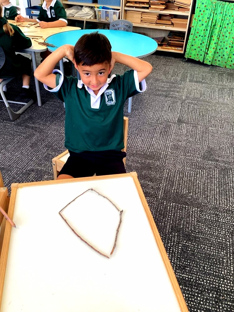 A Prep student creates a large shape using sticks on a tabletop as part of a mathematics activity investigating the properties of 2D shapes.