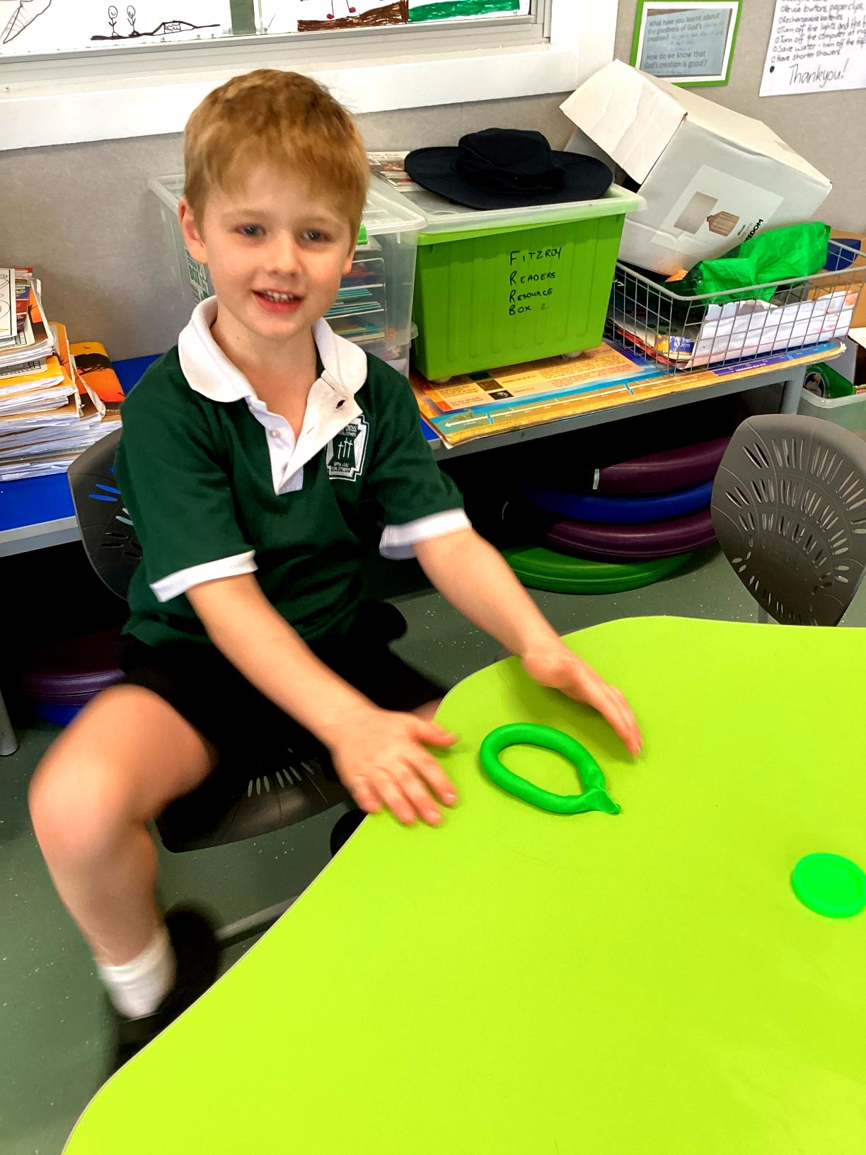 A Prep student uses green modelling clay to form a circular shape while exploring sides, curves and shape properties through hands-on learning.
