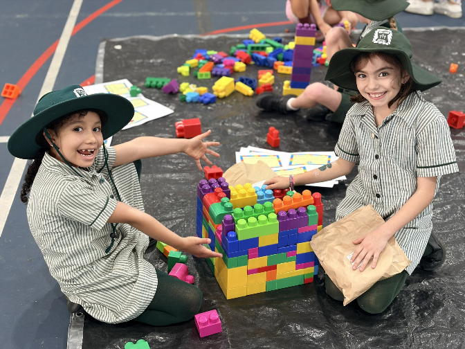 Students in school uniforms build a colourful block structure during a play-based activity.